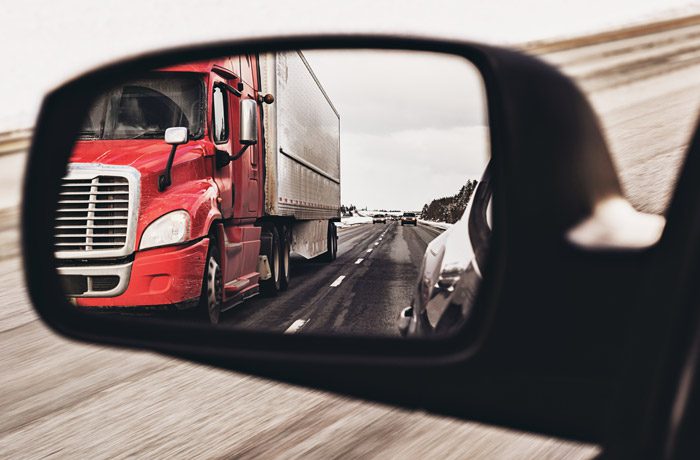 Semi-truck-in-the-rear-view-mirror-of-a-passenger-vehicle